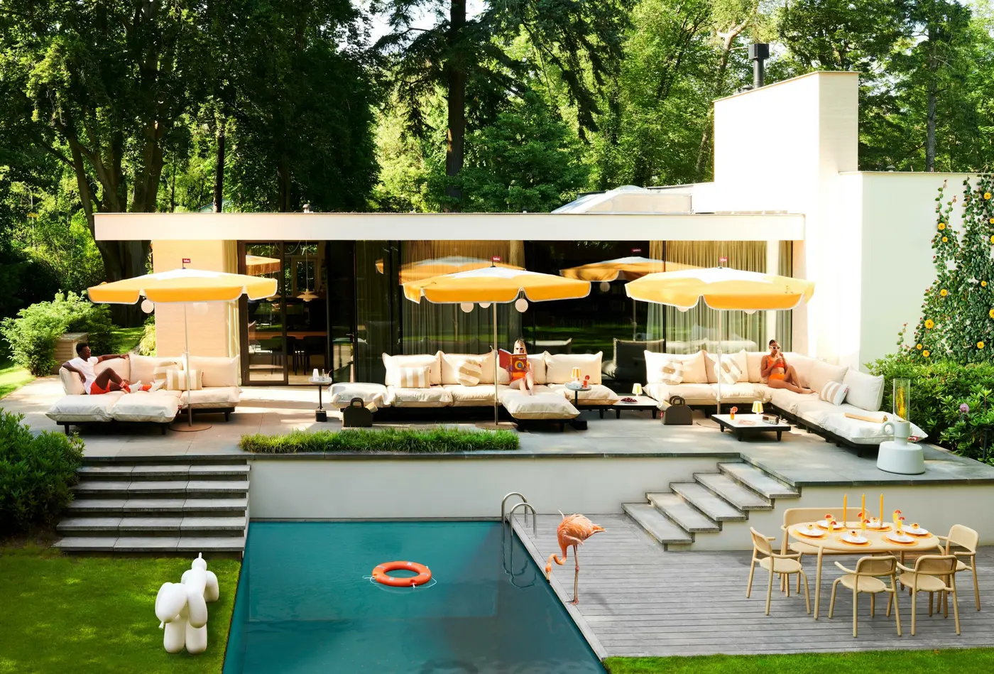 Jardin avec piscine, salon d'extérieur blanc, parasols jaunes et poufs colorés.