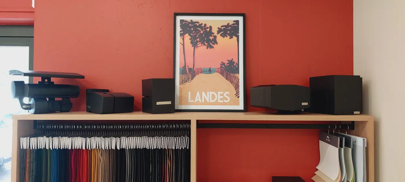 Dans le showroom d'Hossegor : mur rouge, affiche des Landes et étagère d'échantillons de toiles