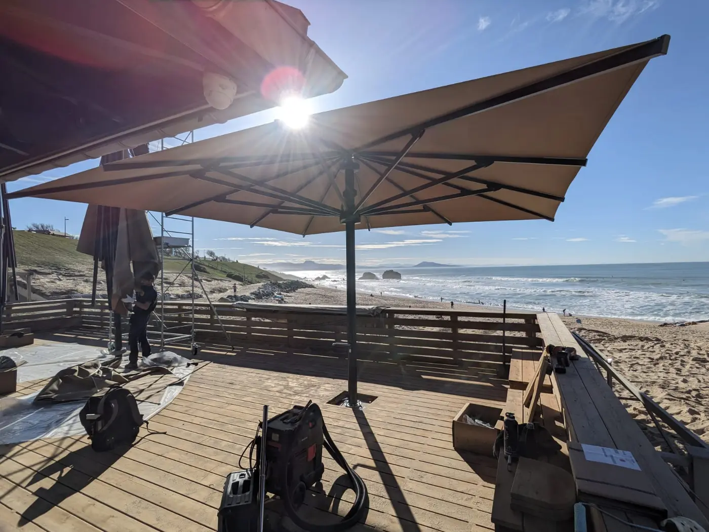 Pose d'un grand parasol sur la terrasse en bois du Milady Beach, face à l'océan