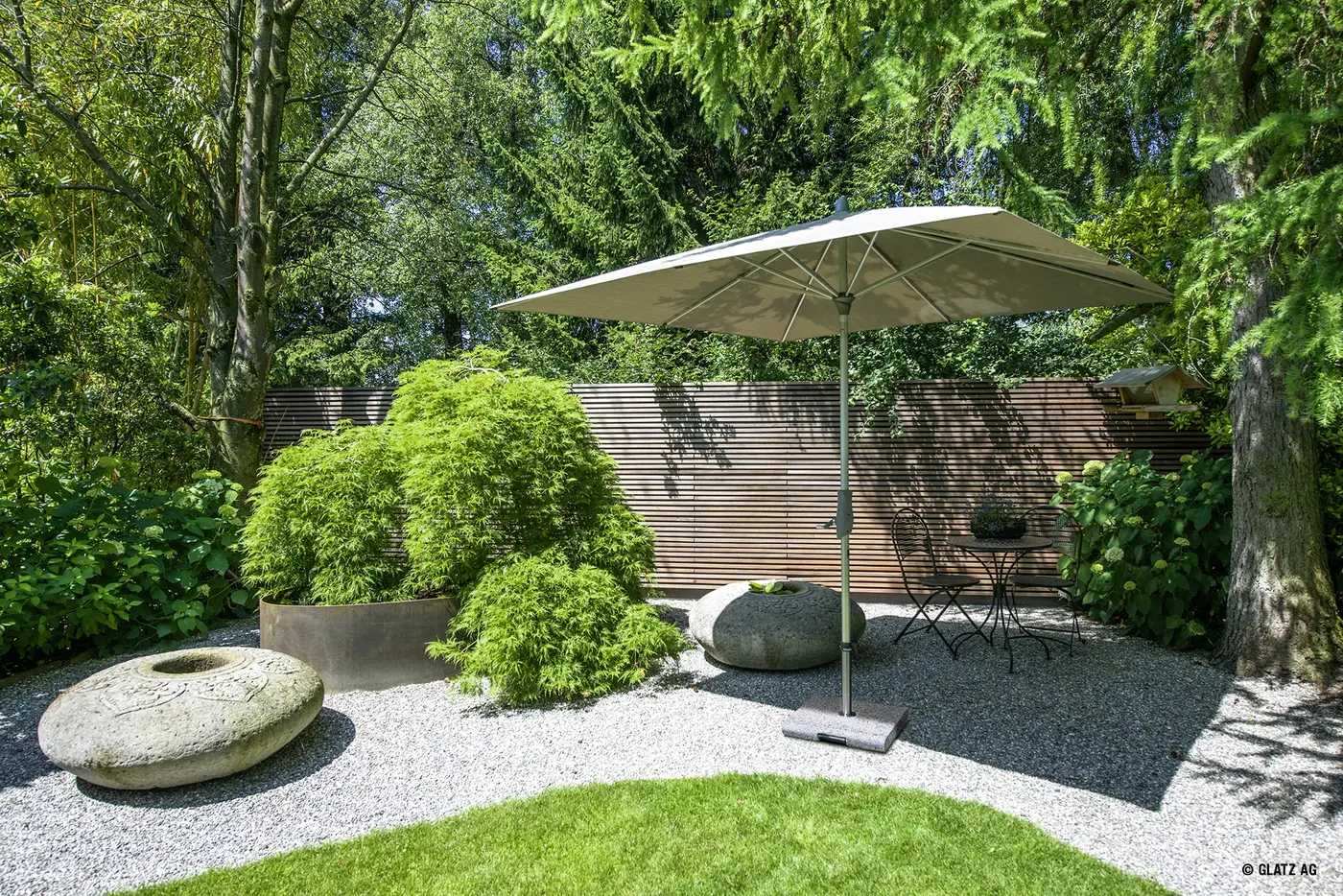 Parasol droit écru au-dessus d'un coin de jardin paysager, avec son pied lesté