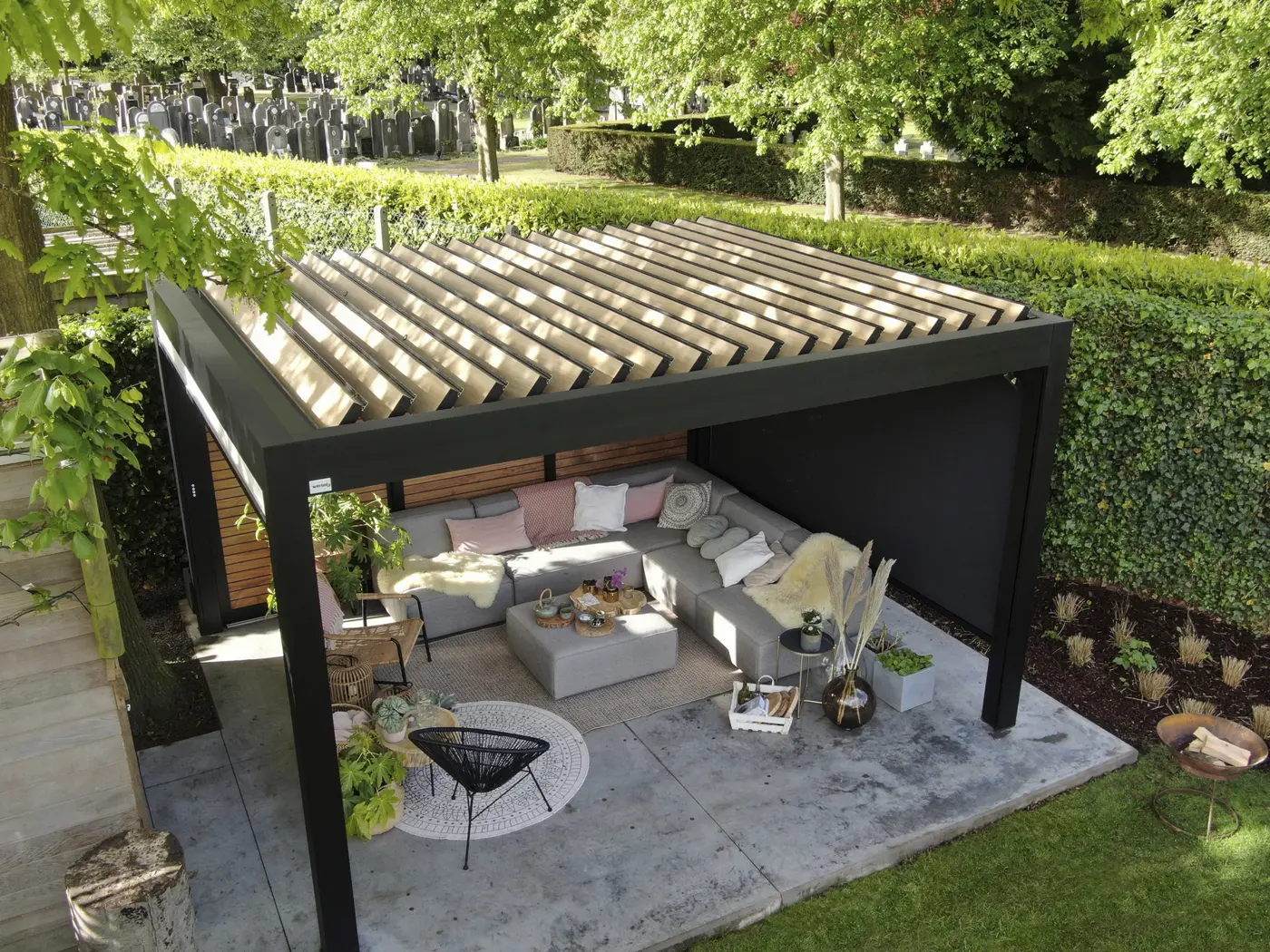 Pergola noire à lames au-dessus d'un salon de jardin, entourée de verdure