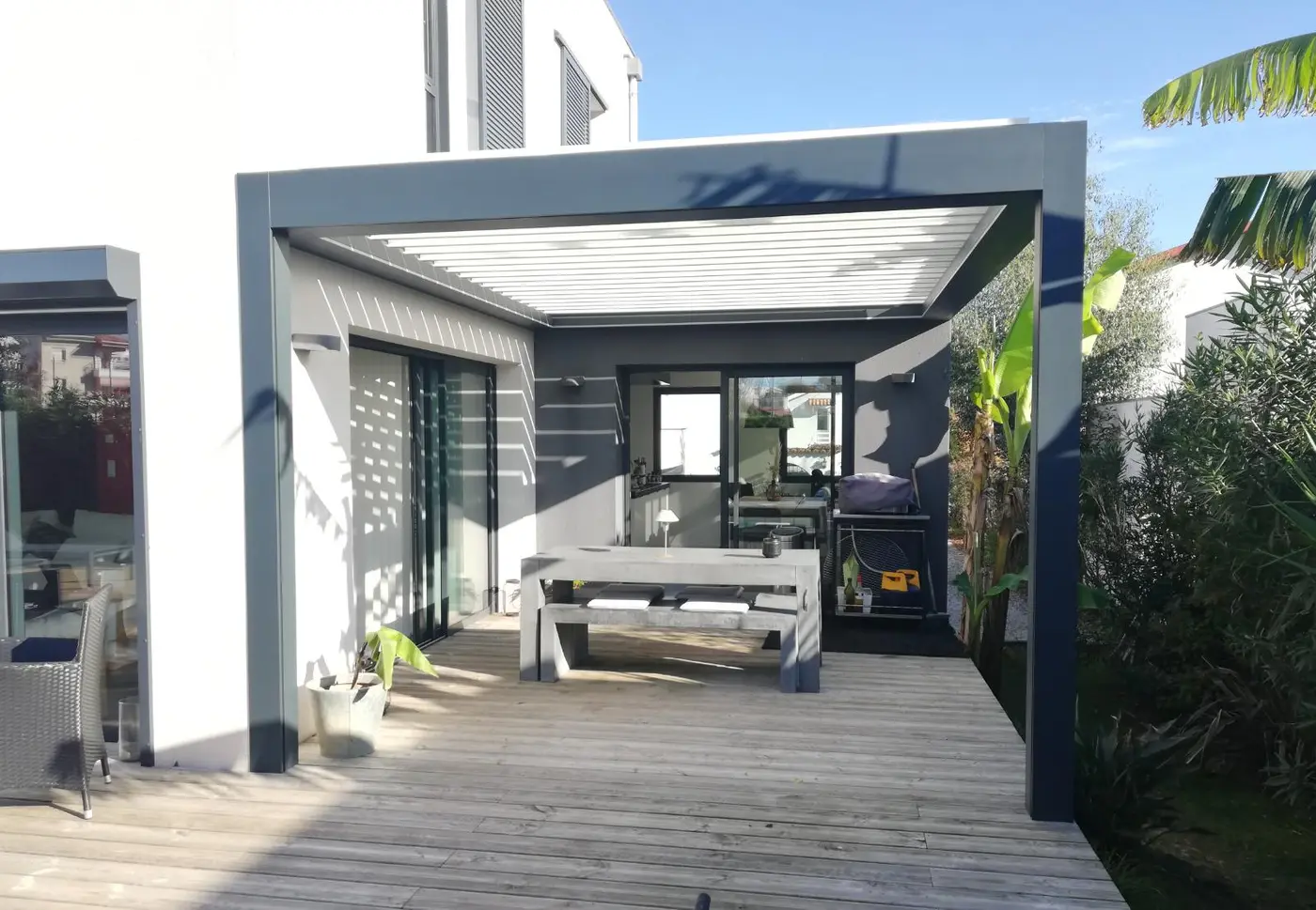 Pergola bioclimatique grise sur une terrasse en bois, table et barbecue à l'abri