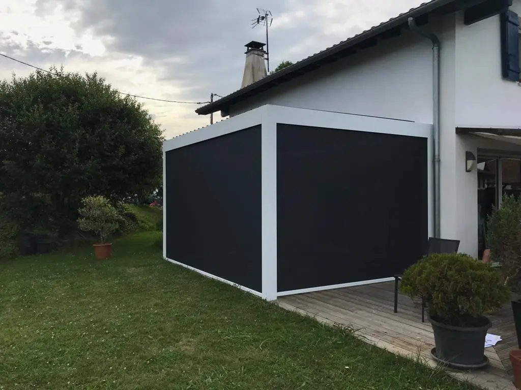 Pergola blanche adossée à une maison à Mouguerre, côtés fermés par des stores verticaux sombres