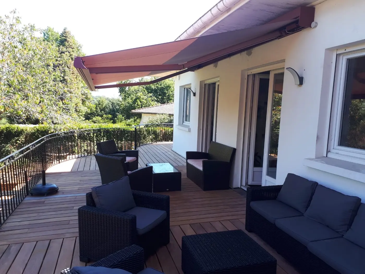 Store banne coffre bordeaux au-dessus d'une terrasse en bois avec salon de jardin