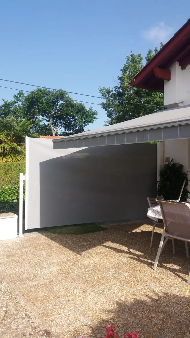 Store latéral gris déroulé sur le côté d'une terrasse pour couper le vent