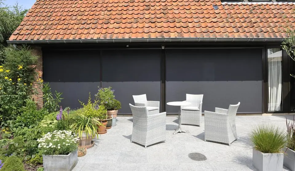 Stores verticaux gris fermés sur un abri de jardin, fauteuils blancs devant