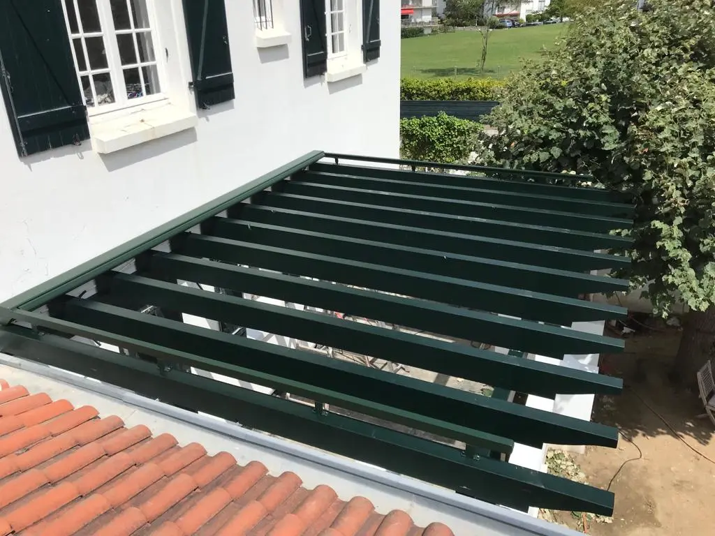 Pergola en bois vert foncé équipée d'un store, vue d'en haut au-dessus d'un toit de tuiles