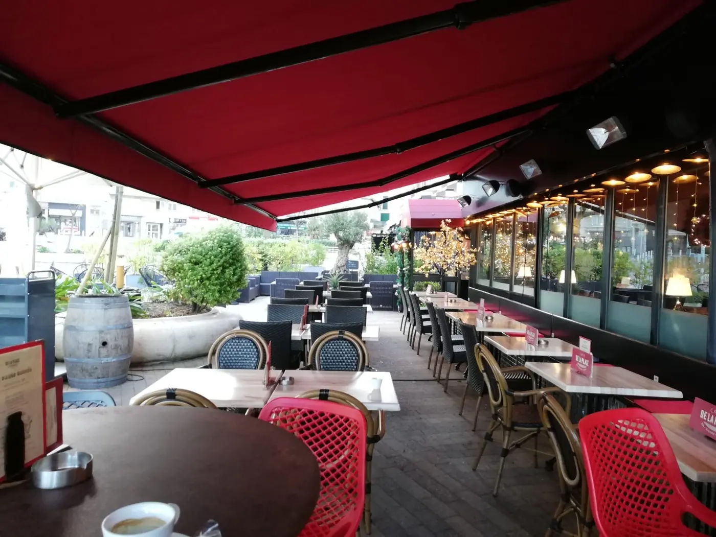 Terrasse couverte du Café de la Place à Biarritz, store rouge déployé au-dessus des tables