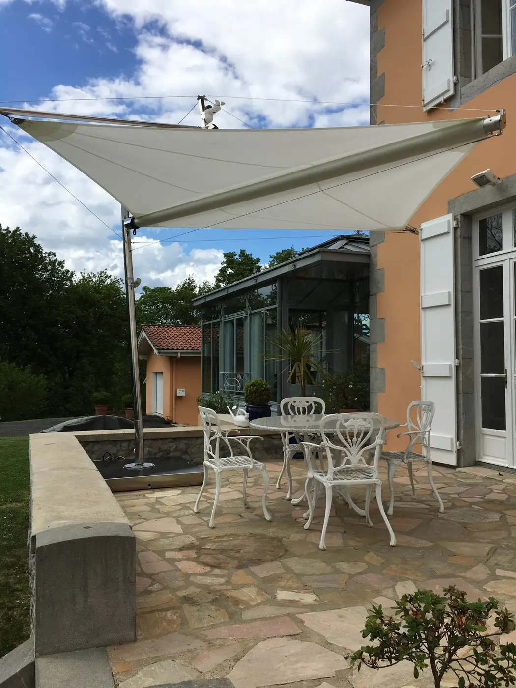 Voile d'ombrage triangulaire au-dessus d'une table de jardin en fer forgé