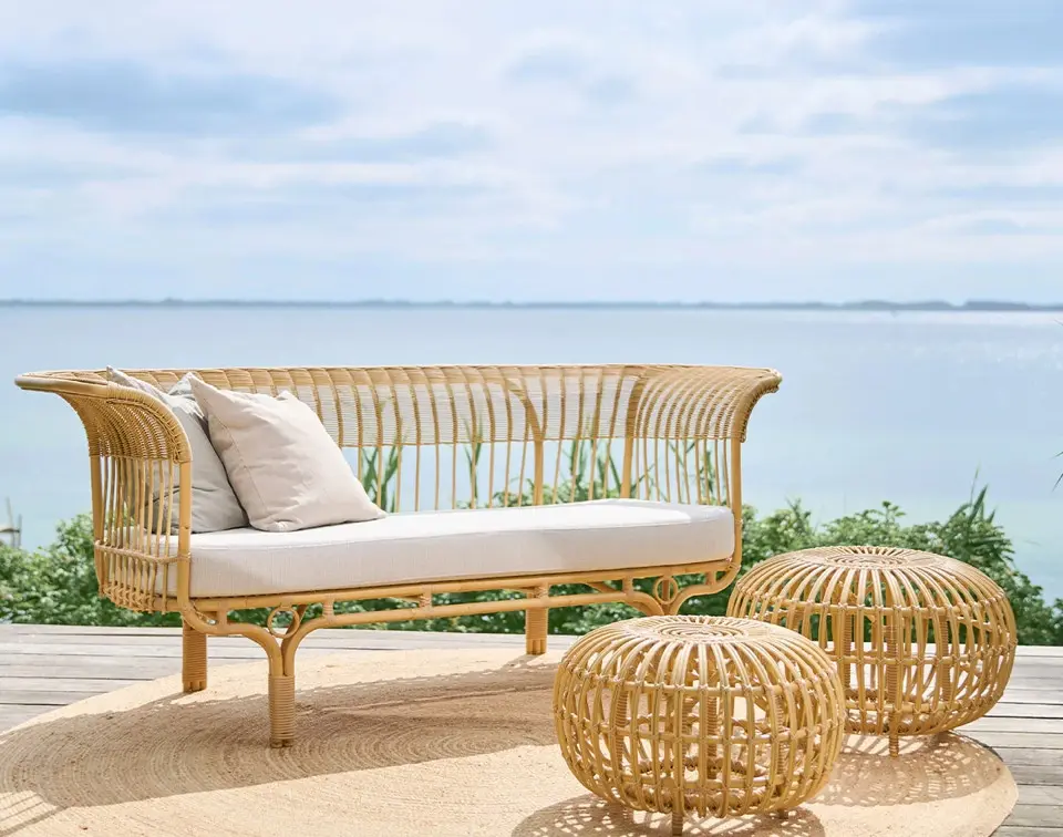 Canapé et poufs en rotin sur une terrasse en bois, face à la mer.